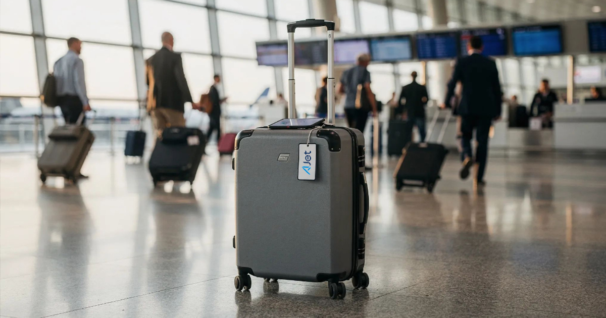 Rolling suitcase with a location tracking tag standing in an airport terminal as travelers walk by in the background.