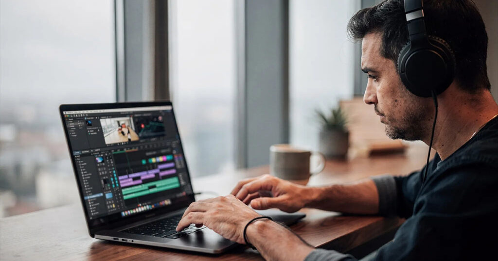 Video editor wearing headphones working on a laptop with video editing software at a desk