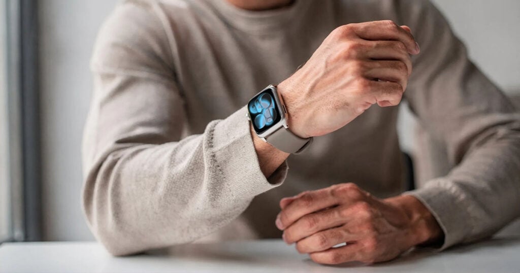 Person wearing an Apple Watch Series 11 with a light band, checking the watch while seated at a table.