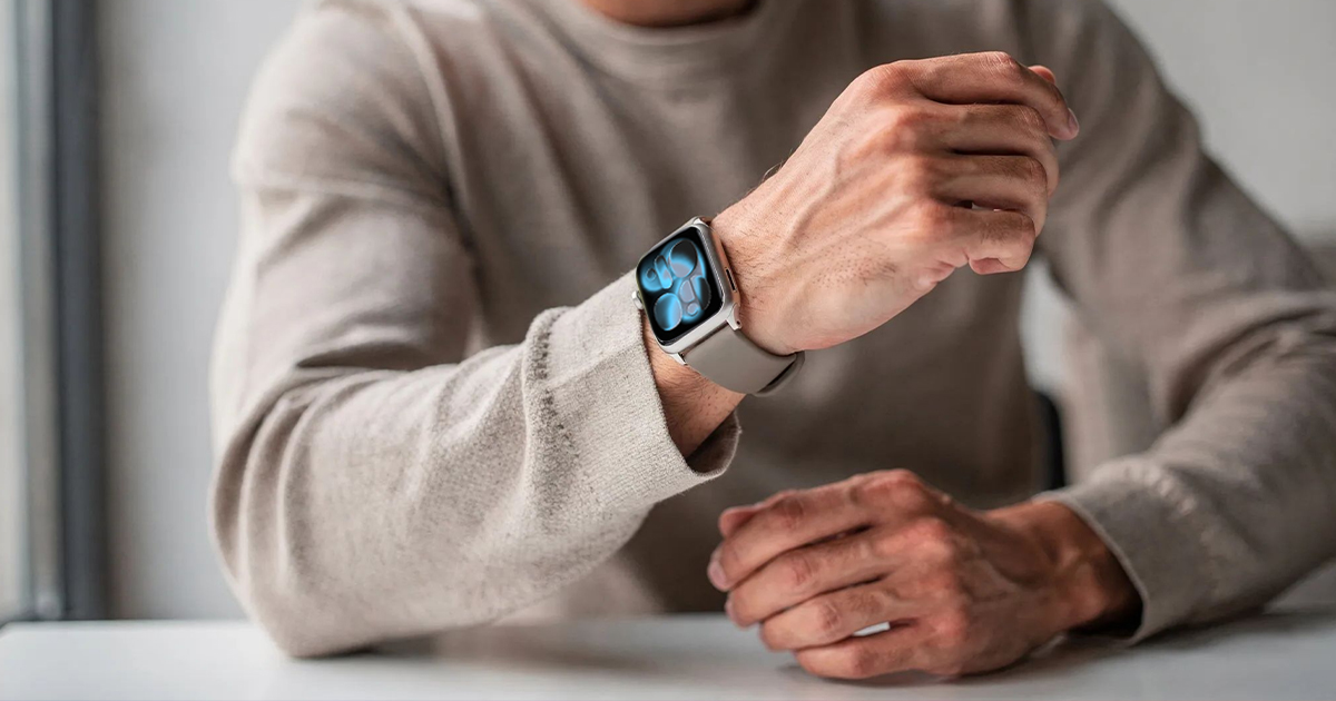 Person wearing an Apple Watch Series 11 with a light band, checking the watch while seated at a table.