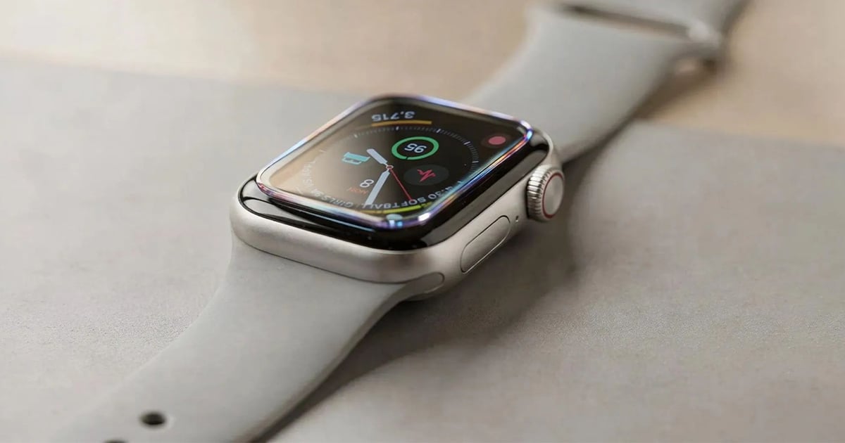 Apple Watch with a glossy white case and matching sport band resting on a light desk surface, its display showing an activity watch face with colorful rings and step count.