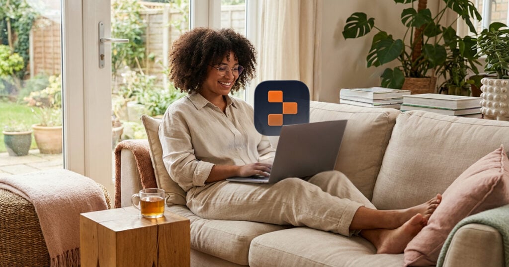 Smiling woman working on a laptop while relaxing on a sofa in a bright, plant-filled living room
