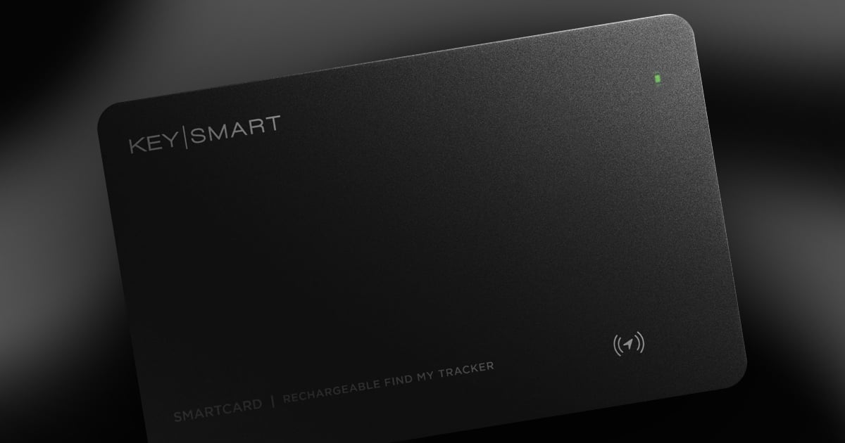 Matte black KeySmart SmartCard tracker angled on a dark background, showing the KEY|SMART logo, a small green charge indicator light, a wireless signal icon, and "SmartCard | Rechargeable Find My Tracker" text.