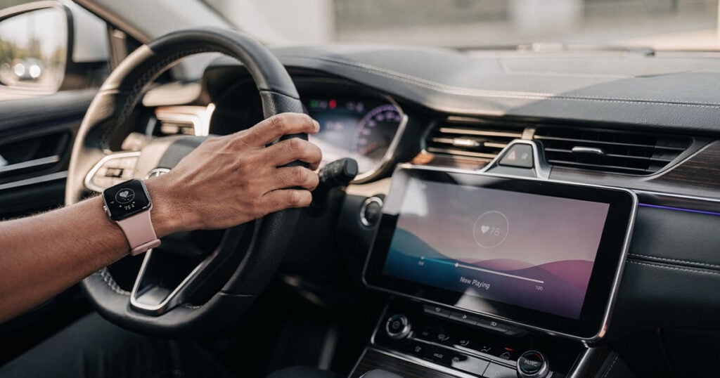 Driver using Apple CarPlay on a modern car dashboard touchscreen while wearing a smartwatch.