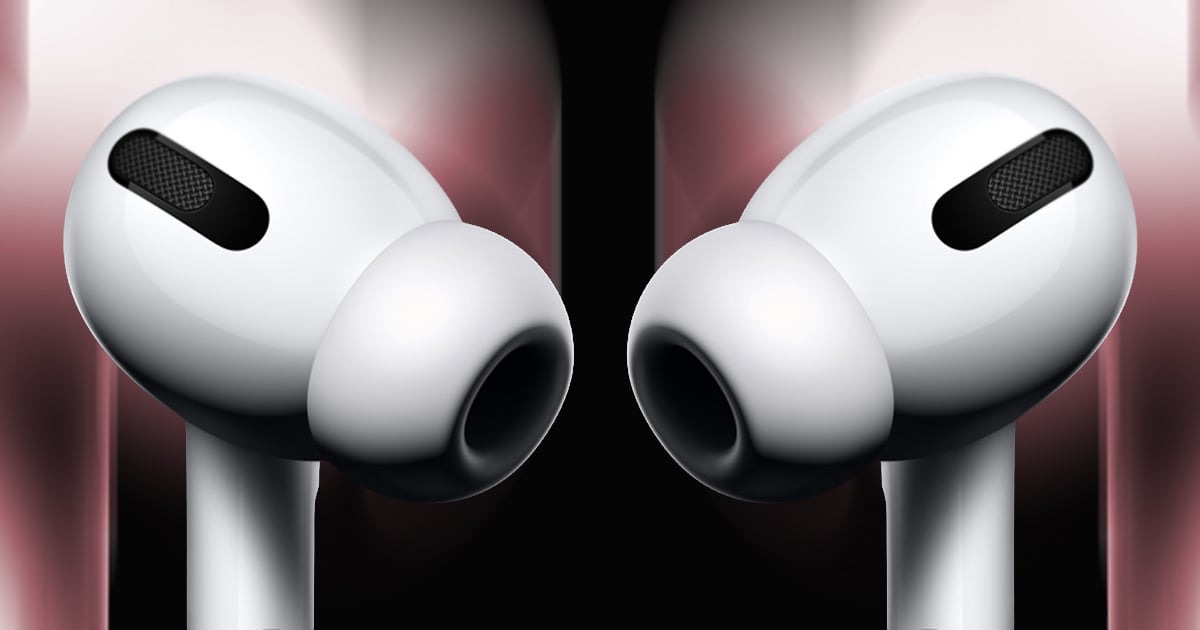 Extreme close-up of a pair of white AirPods Pro facing each other, silicone ear tips and mesh microphone vents visible against a dark background with soft red and pink lighting.